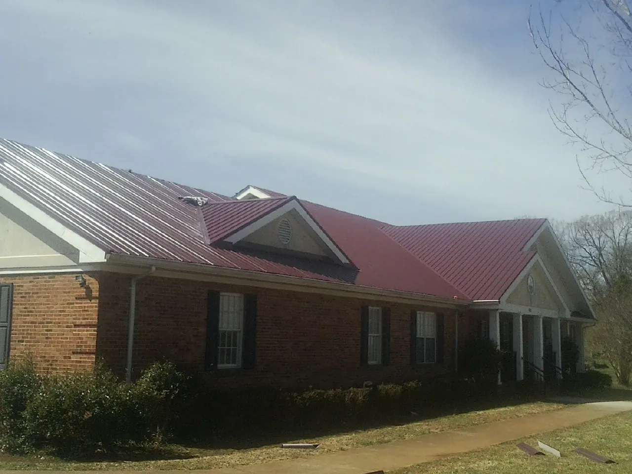 Red metal roof with gabled entries on a long brick building, from a Hail Damage Roof Repair job in Delavan