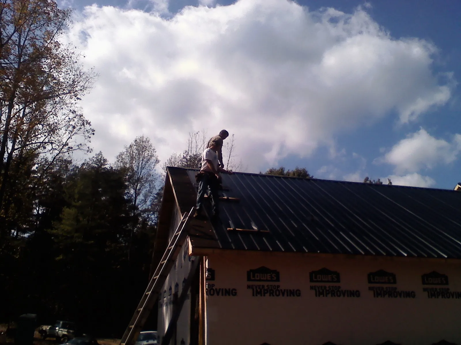 Roofer fastening dark metal panels high against a cloudy sky, from a Roof Inspection job in Delavan